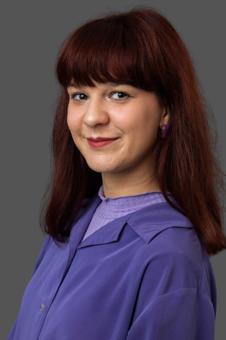 Portrait of a woman with shoulder-length auburn hair, wearing a purple blouse, smiling softly.